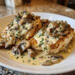 Two golden-brown chicken breasts smothered in a rich, creamy mushroom sauce and garnished with fresh parsley.