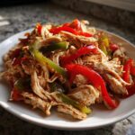 A close-up of shredded chicken mixed with sliced red and green bell peppers, seasoned for Crockpot Chicken Fajitas.