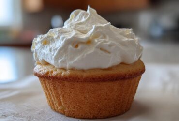 A single vanilla cupcake topped with a generous swirl of fluffy white Cool Whip frosting.