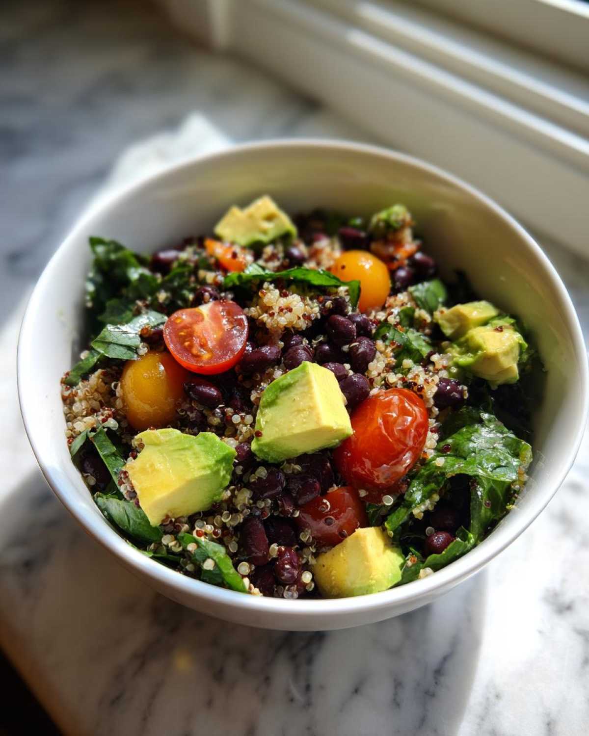 A vibrant close-up of a Fresh Avocado Bowl featuring quinoa, black beans, cherry tomatoes, and chunks of avocado.