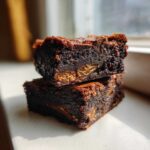 Two fudgy, dark chocolate Kit Kat Brownies stacked on top of each other, showing the crispy wafer filling inside.
