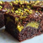 Close-up of a fudgy Pistachio Dubai Brownies square showing the rich chocolate cake and bright green pistachio swirl center, topped with chopped pistachios.