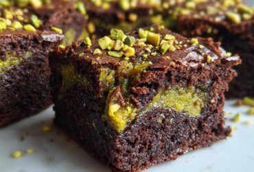 Close-up of a fudgy Pistachio Dubai Brownies square showing the rich chocolate cake and bright green pistachio swirl center, topped with chopped pistachios.