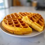 Close-up of golden brown High Protein Waffles stacked on a white plate, showing the fluffy interior texture.