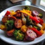 A white bowl filled with caramelized slices of Honey Garlic Kielbasa & Veggies, including broccoli, peppers, and onions.