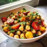 Close-up of a vibrant Mediterranean Diet Chickpea Salad featuring chickpeas, halved cherry tomatoes, and fresh herbs in a white bowl.