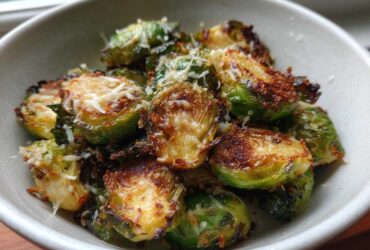 Close-up of crispy Oven Roasted Brussels Sprouts with Parmesan served in a light-colored bowl.