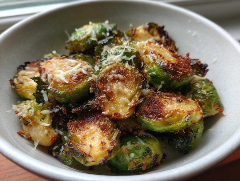Close-up of crispy Oven Roasted Brussels Sprouts with Parmesan served in a light-colored bowl.