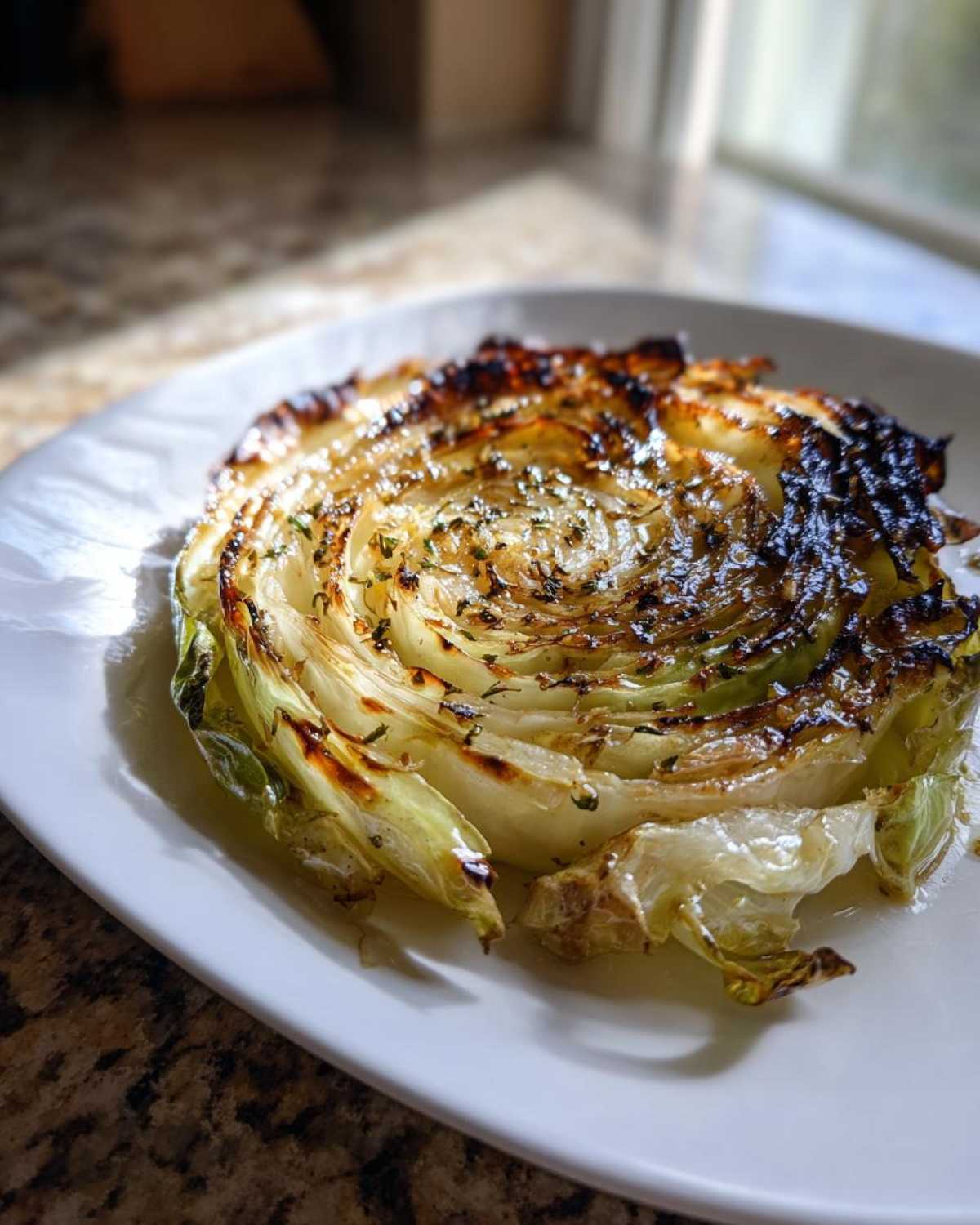 A single, beautifully charred Oven Roasted Garlic Cabbage Steak seasoned with herbs on a white plate.