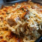 A spoonful of creamy Chicken Orzo Bake lifted from the pan, showing tender chicken and melted, bubbly cheese topping.