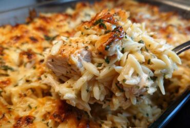 A spoonful of creamy Chicken Orzo Bake lifted from the pan, showing tender chicken and melted, bubbly cheese topping.