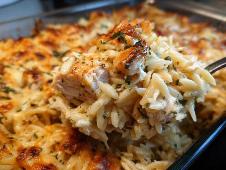 A spoonful of creamy Chicken Orzo Bake lifted from the pan, showing tender chicken and melted, bubbly cheese topping.