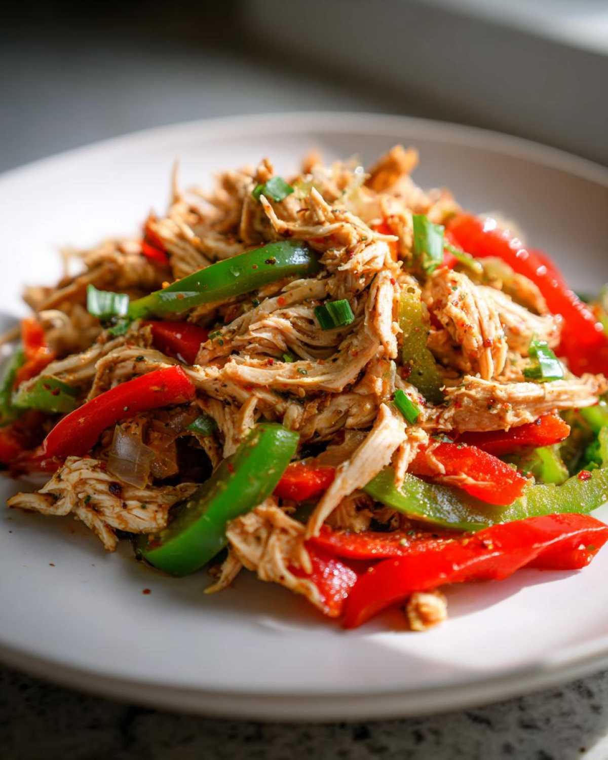 Close-up of shredded chicken mixed with sliced red and green bell peppers, ready for Crockpot Chicken Fajitas.