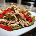 Shredded chicken mixed with sliced red and green bell peppers, ready for Crockpot Chicken Fajitas.