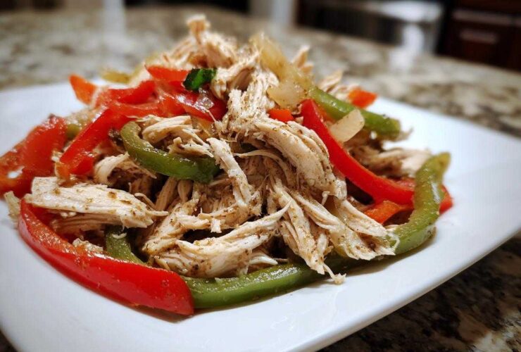 Shredded chicken mixed with sliced red and green bell peppers, ready for Crockpot Chicken Fajitas.