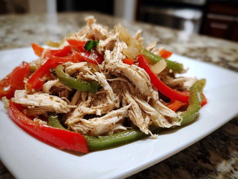 Shredded chicken mixed with sliced red and green bell peppers, ready for Crockpot Chicken Fajitas.