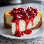 A decadent slice of Strawberry Cheesecake with a thick graham cracker crust and rich strawberry topping dripping down the side.
