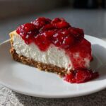 A perfect slice of creamy Strawberry Cheesecake with a thick graham cracker crust and bright red strawberry topping.