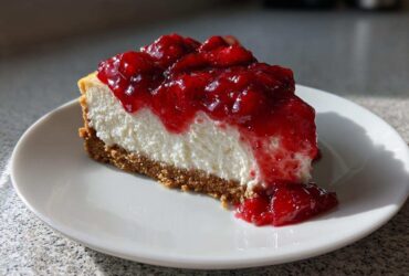 A perfect slice of creamy Strawberry Cheesecake with a thick graham cracker crust and bright red strawberry topping.
