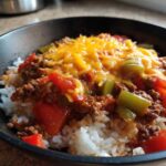 Close-up of Unstuffed Pepper Skillet mixture with ground beef, tomatoes, green peppers, and melted cheddar cheese served over white rice in a black bowl.