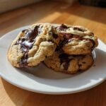 Three freshly baked Cream Cheese Chocolate Chip Cookies stacked on a white plate with melted chocolate.