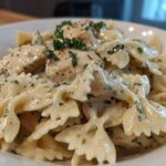 A close-up shot of a bowl filled with Creamy Chicken Bowtie Pasta, coated in a rich white sauce and garnished with fresh parsley.