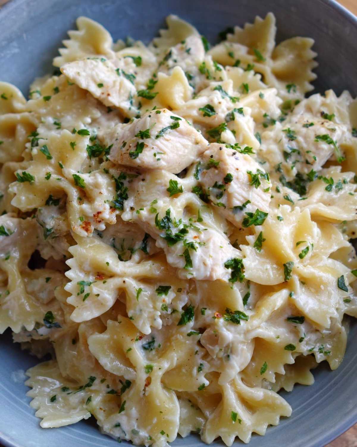 A close-up view of a bowl filled with rich Creamy Chicken Bowtie Pasta, topped with fresh parsley.