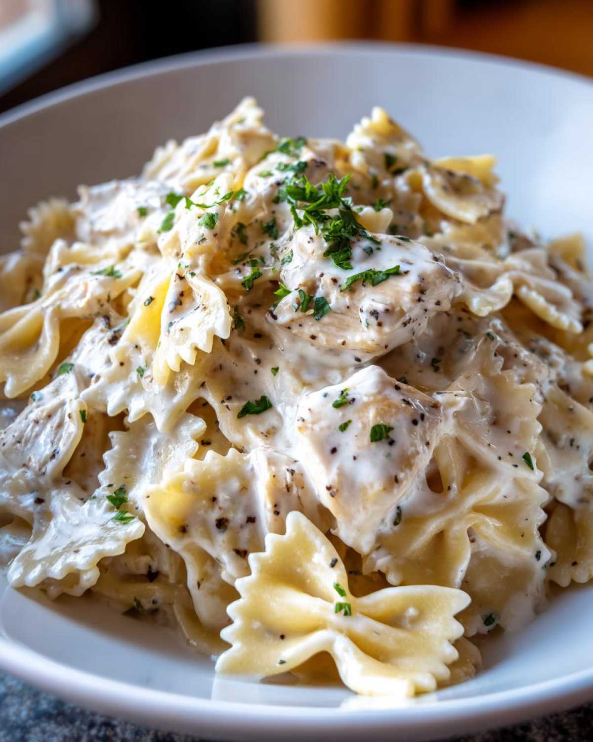 A close-up shot of rich Creamy Chicken Bowtie Pasta coated in a white sauce and sprinkled with black pepper and parsley.