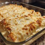 Close-up of freshly baked Creamy White Chicken Enchiladas covered in melted, slightly browned cheese sauce in a glass baking dish.