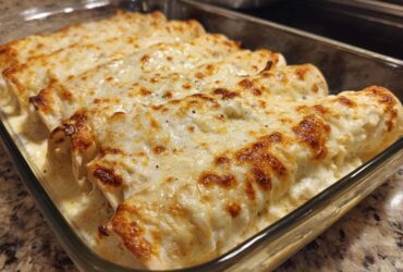 Close-up of freshly baked Creamy White Chicken Enchiladas covered in melted, slightly browned cheese sauce in a glass baking dish.