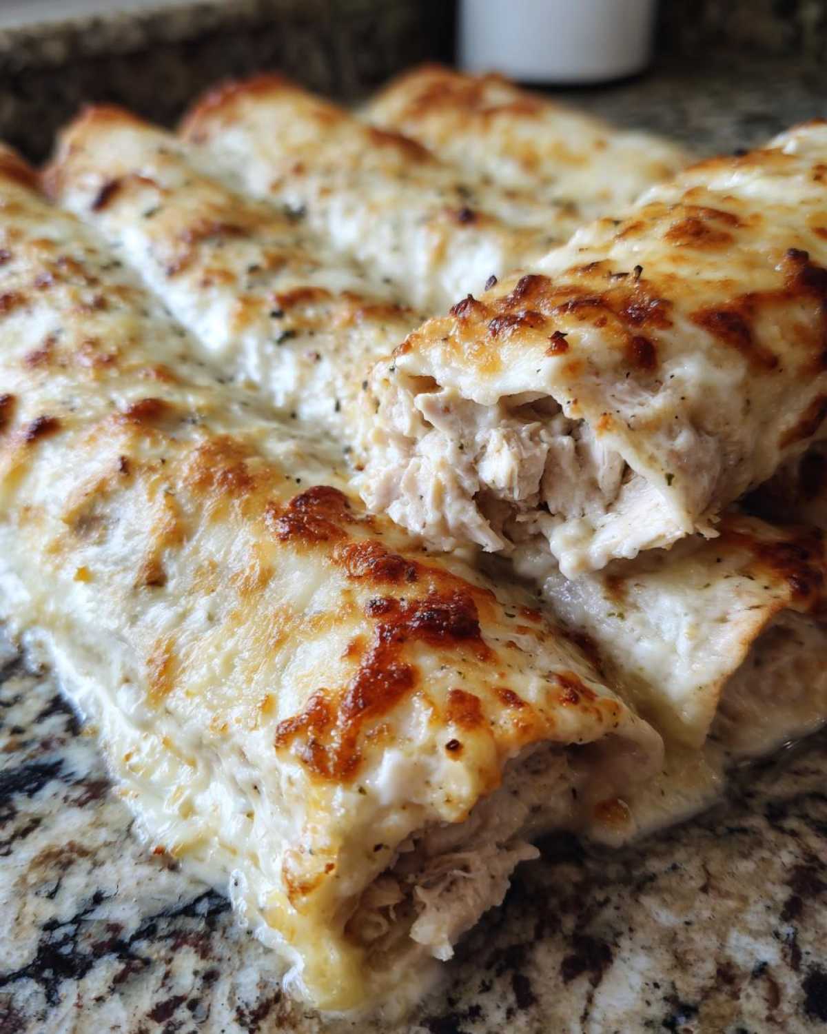 Close-up of baked Creamy White Chicken Enchiladas covered in melted, browned cheese, showing shredded chicken filling.