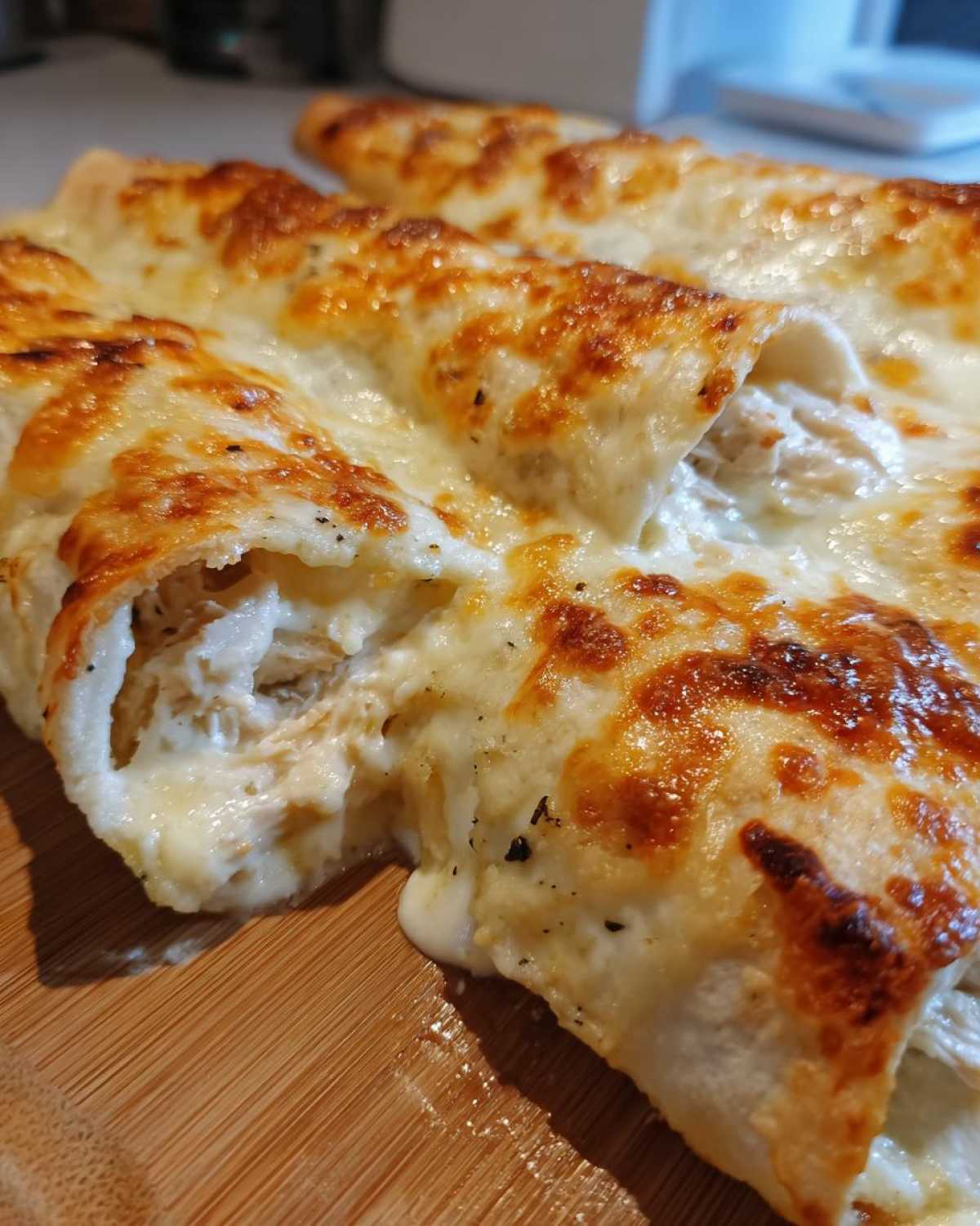 Close-up of freshly baked Creamy White Chicken Enchiladas with melted, browned cheese topping and visible shredded chicken filling.