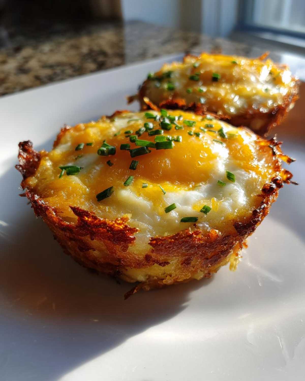 Close-up of two crispy Hash Brown Breakfast Cups topped with a baked egg and fresh chives.