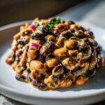 Close-up of a mound of Dense Bean Salad featuring black and light-colored beans coated in a thick, creamy orange dressing, garnished with red onion and parsley.