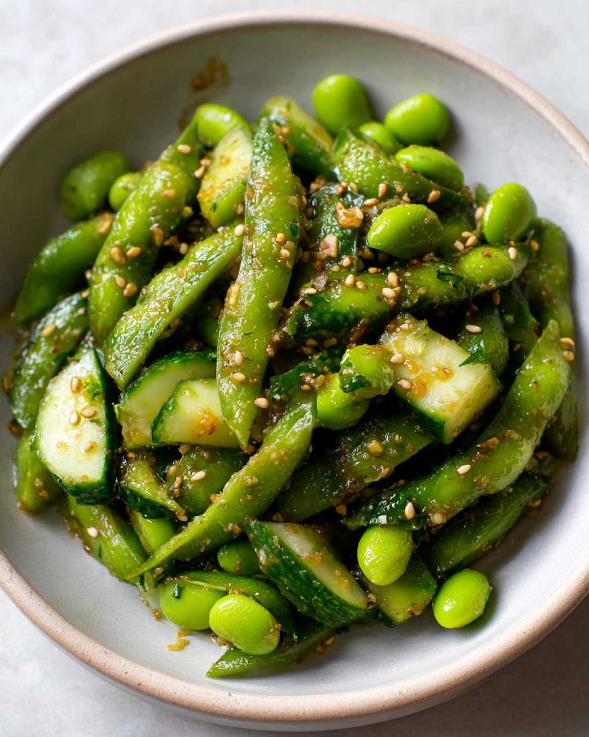 Close-up of a vibrant Edamame and Cucumber Salad tossed in a savory dressing with sesame seeds.
