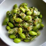 Close-up of vibrant Edamame and Cucumber Salad tossed with sesame seeds and herbs in a white bowl.