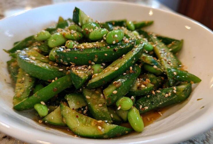 A close-up of a bright green Edamame and Cucumber Salad tossed in a savory dressing and topped with sesame seeds.