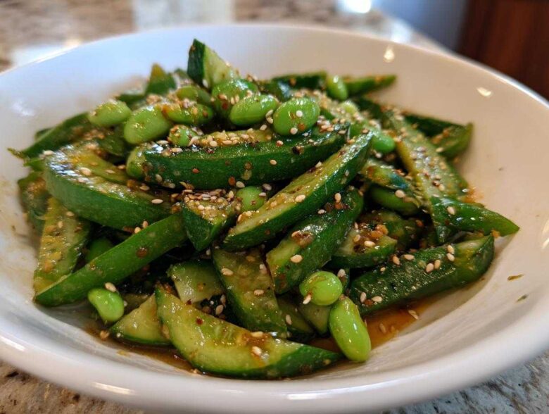 A close-up of a bright green Edamame and Cucumber Salad tossed in a savory dressing and topped with sesame seeds.