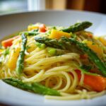 A close-up, featured image of bright Pasta Primavera featuring spaghetti tossed with bright green asparagus and orange bell peppers.