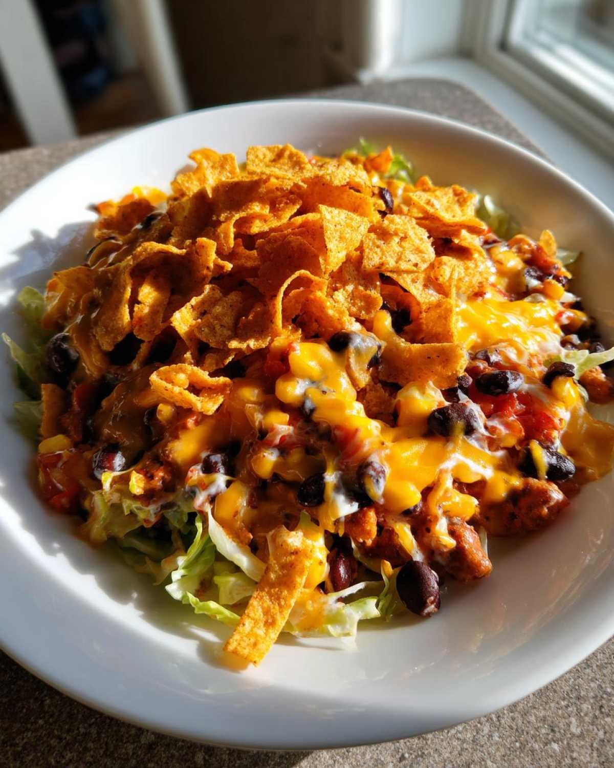A close-up of a Frito Cowboy Cabbage Salad in a white bowl, topped with melted cheese, black beans, and Fritos corn chips.