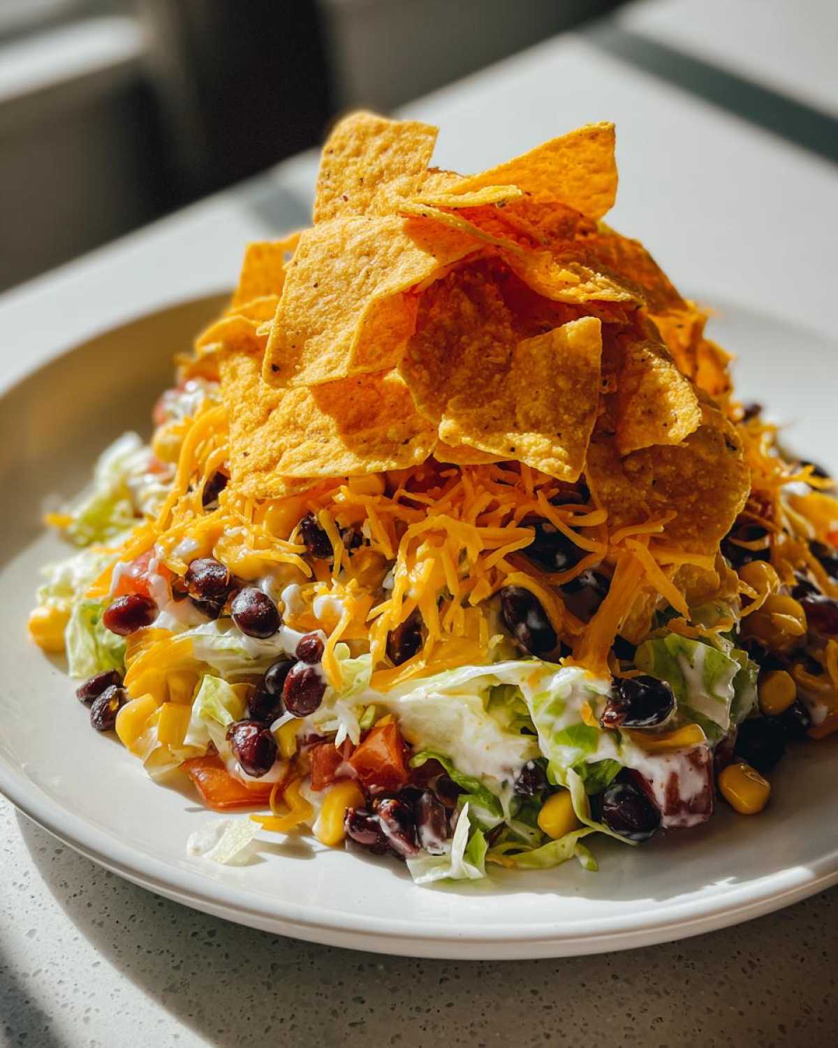 A tall serving of Frito Cowboy Cabbage Salad topped with shredded cheese, black beans, corn, and a mountain of tortilla chips.
