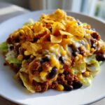 A close-up serving of Frito Cowboy Cabbage Salad featuring lettuce, seasoned ground beef, black beans, corn, melted cheese, and Fritos on top.