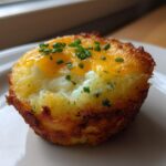 A single, crispy Hash Brown Breakfast Cup topped with melted cheddar cheese and fresh chives, resting on a white plate.