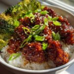 Close-up of a Honey BBQ Chicken Rice Bowl featuring glazed chicken pieces over white rice, topped with sesame seeds and green onions, served with roasted broccoli.