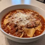 Close-up of a white bowl filled with rich, tomato-based Lasagna Soup topped generously with ground meat and grated Parmesan cheese.