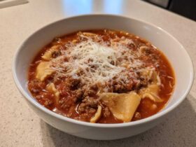 Close-up of a white bowl filled with rich, tomato-based Lasagna Soup topped generously with ground meat and grated Parmesan cheese.