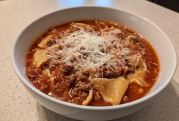 Close-up of a white bowl filled with rich, tomato-based Lasagna Soup topped generously with ground meat and grated Parmesan cheese.