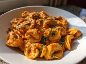 Close-up of Marry Me Tortellini coated in a rich, creamy orange sauce with spinach and black pepper.