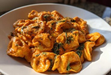 Close-up of Marry Me Tortellini coated in a rich, creamy orange sauce with spinach and black pepper.