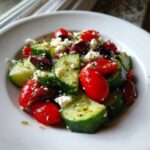 A close-up of a vibrant Mediterranean Cucumber Salad featuring sliced cucumbers, cherry tomatoes, Kalamata olives, and crumbled feta cheese.